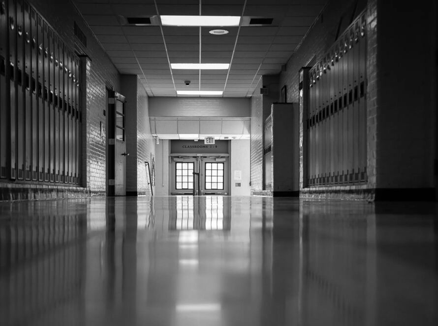 Corredor vazio de uma escola pública com luz natural entrando pelas janelas, portas fechadas e atmosfera silenciosa que transmite abandono e passagem do tempo