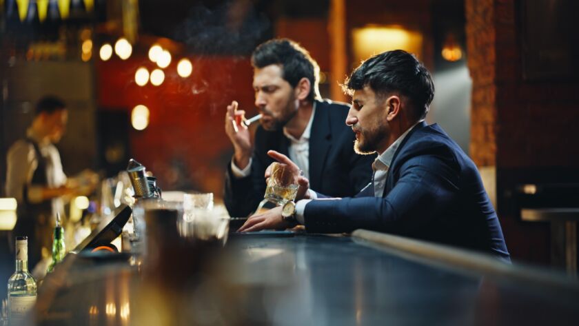 dois amigos adultos sentados em silêncio à mesa com clima contemplativo e distância emocional